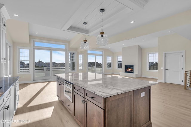 kitchen with a glass covered fireplace, stainless steel microwave, hanging light fixtures, and light wood finished floors