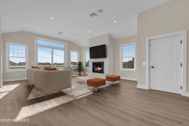 living room featuring visible vents, a glass covered fireplace, wood finished floors, baseboards, and lofted ceiling