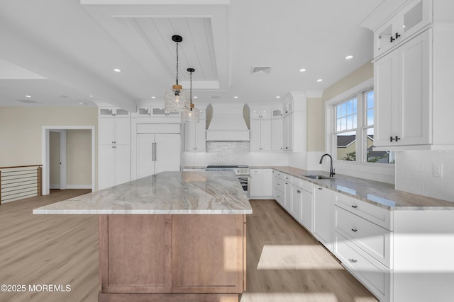 kitchen featuring light wood-type flooring, a sink, paneled built in fridge, gas range, and custom exhaust hood