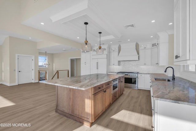 kitchen with light wood finished floors, visible vents, premium range hood, built in appliances, and a sink