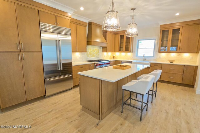 kitchen featuring a kitchen bar, light wood-type flooring, premium range hood, premium appliances, and a center island