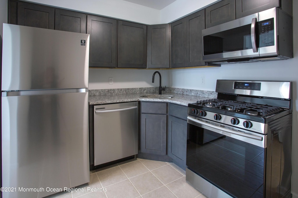 kitchen featuring sink, light stone countertops, dark brown cabinets, light tile patterned flooring, and stainless steel appliances