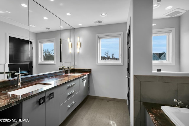 bathroom featuring double vanity, a washtub, visible vents, and a sink