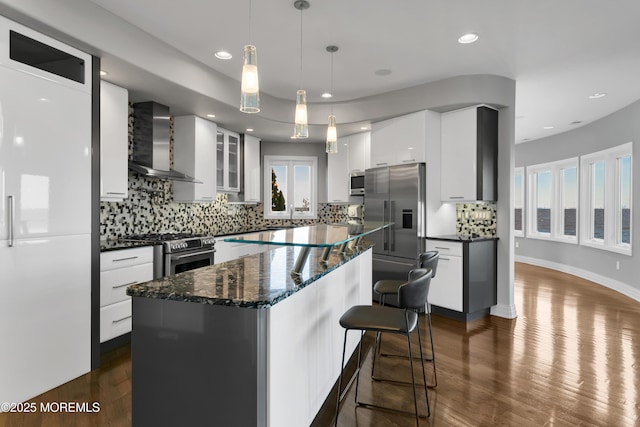 kitchen with dark wood-type flooring, a kitchen island, white cabinetry, stainless steel appliances, and wall chimney range hood