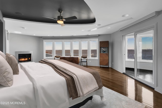 bedroom featuring baseboards, recessed lighting, wood finished floors, a glass covered fireplace, and access to outside