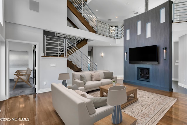 living room with stairway, wood finished floors, baseboards, and a towering ceiling