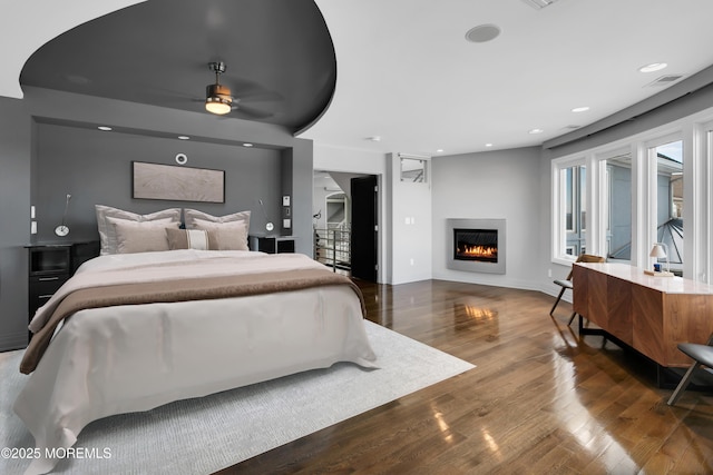 bedroom with visible vents, baseboards, recessed lighting, wood finished floors, and a glass covered fireplace