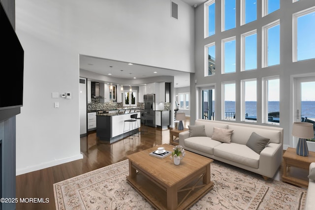 living room with dark wood-style floors, visible vents, baseboards, recessed lighting, and a water view