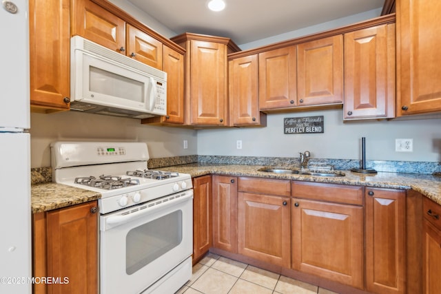 kitchen with white appliances, light stone countertops, sink, and light tile patterned floors