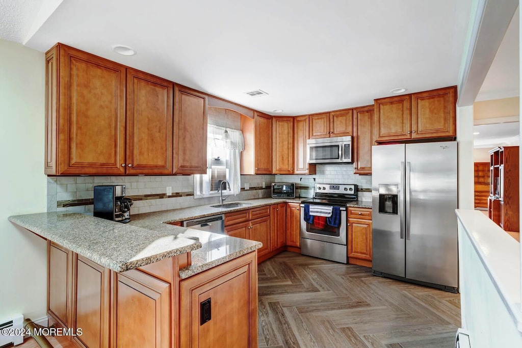 kitchen featuring sink, dark parquet flooring, light stone counters, kitchen peninsula, and stainless steel appliances