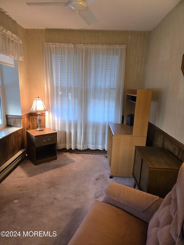 interior space featuring carpet, ceiling fan, wooden walls, and a baseboard radiator