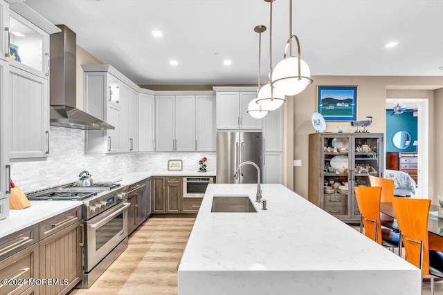 kitchen featuring pendant lighting, a center island with sink, high end appliances, and wall chimney range hood