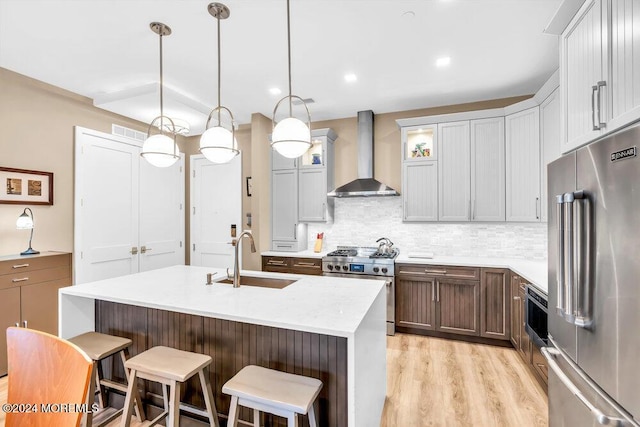 kitchen with wall chimney exhaust hood, high end appliances, sink, pendant lighting, and light hardwood / wood-style floors