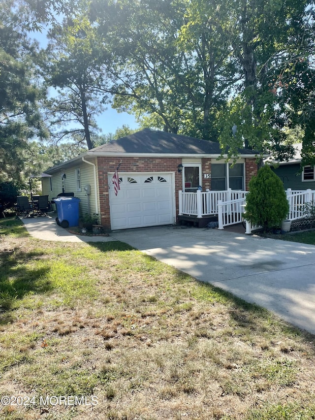 single story home with a porch, a garage, brick siding, concrete driveway, and a front lawn