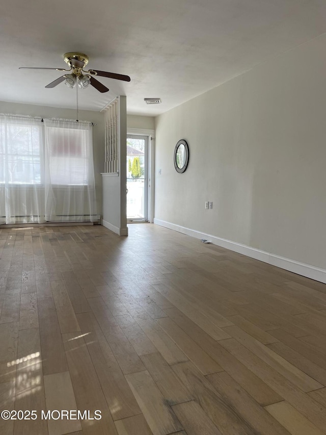 spare room featuring ceiling fan, a baseboard radiator, wood finished floors, visible vents, and baseboards