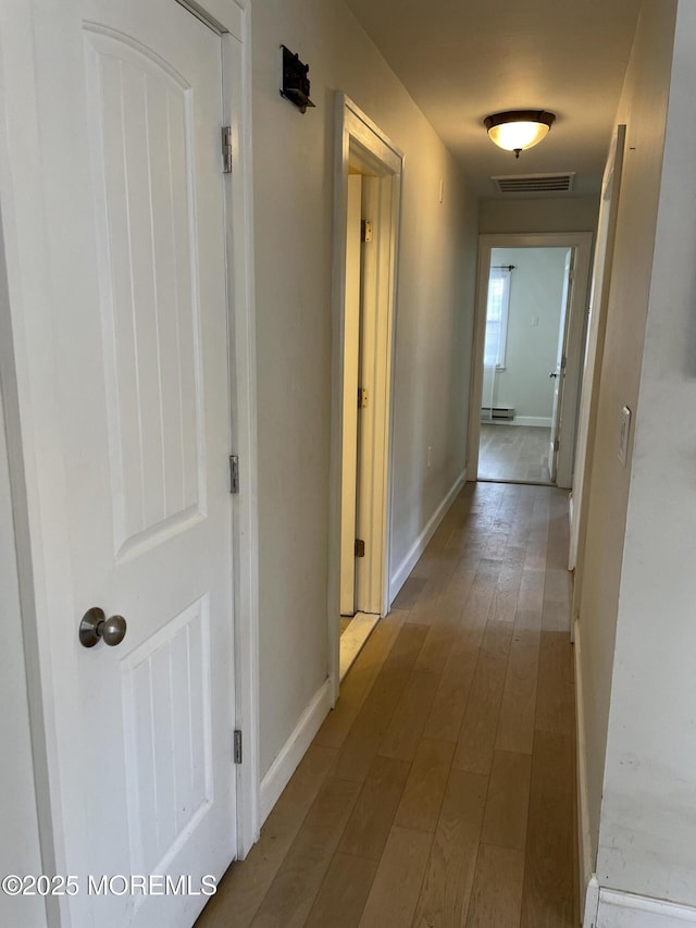 corridor featuring visible vents, baseboards, and wood finished floors