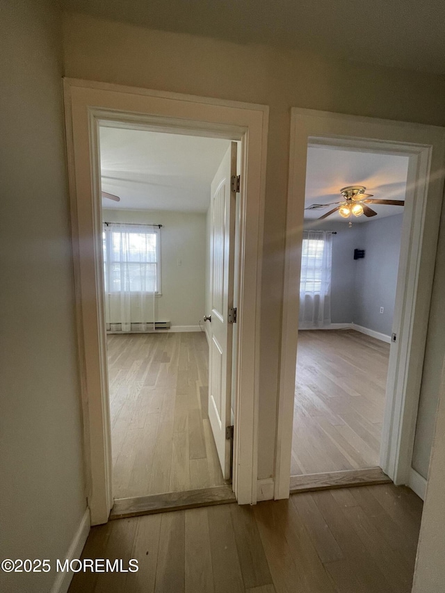 hallway with wood-type flooring, baseboards, baseboard heating, and a wealth of natural light