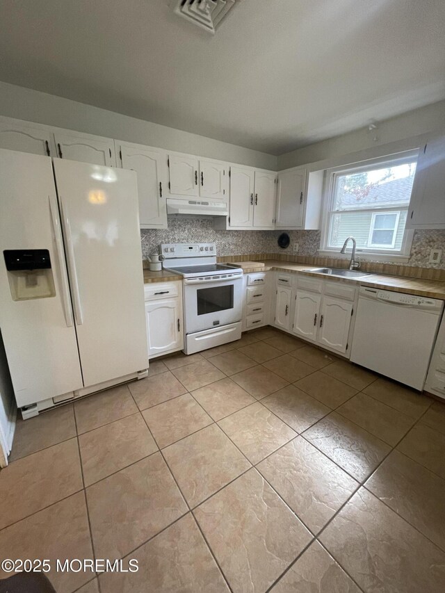 kitchen featuring white appliances, a sink, under cabinet range hood, white cabinetry, and backsplash