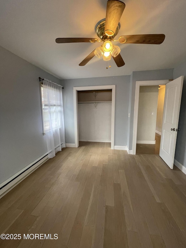 unfurnished bedroom featuring a closet, baseboard heating, a ceiling fan, wood finished floors, and baseboards