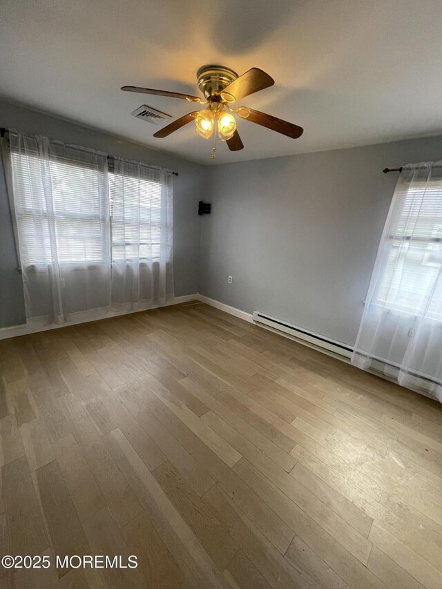 unfurnished room with baseboards, wood finished floors, visible vents, and a healthy amount of sunlight