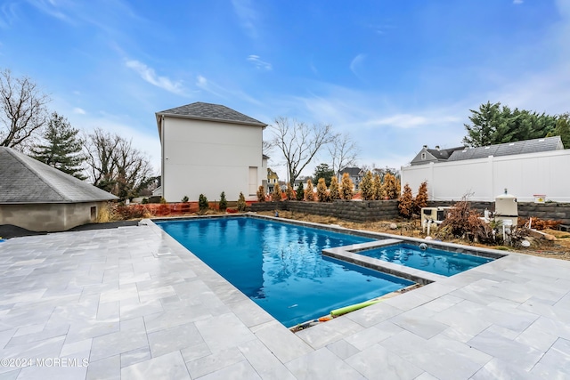 view of pool with a pool with connected hot tub, a patio area, and fence