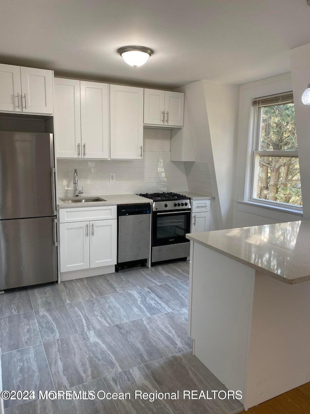 kitchen with appliances with stainless steel finishes, white cabinetry, a sink, and decorative backsplash