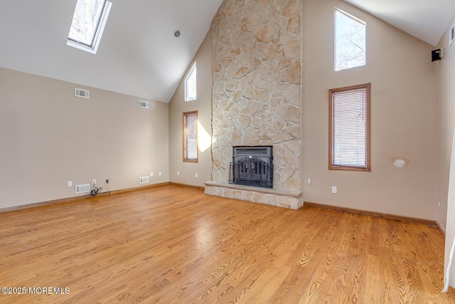 unfurnished living room with a fireplace, light wood-type flooring, a skylight, and a healthy amount of sunlight