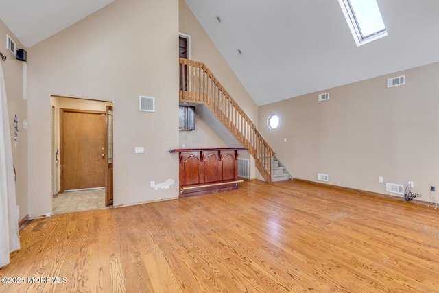 unfurnished living room featuring a skylight, high vaulted ceiling, and light hardwood / wood-style floors