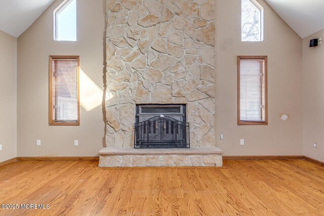 unfurnished living room with a stone fireplace, plenty of natural light, light hardwood / wood-style floors, and lofted ceiling