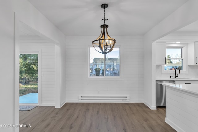 unfurnished dining area with a chandelier, sink, hardwood / wood-style floors, and a baseboard heating unit