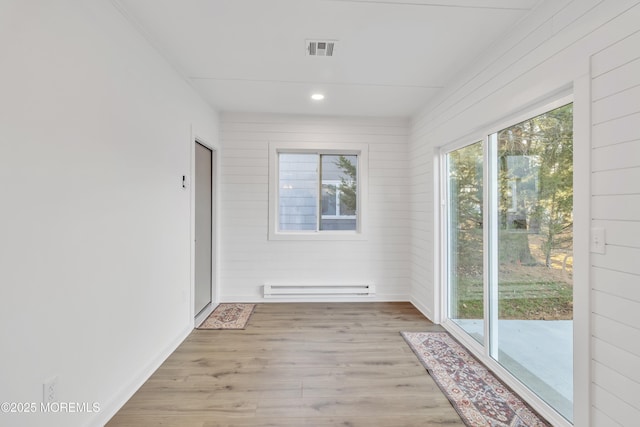 unfurnished room featuring baseboard heating, light hardwood / wood-style flooring, and wood walls