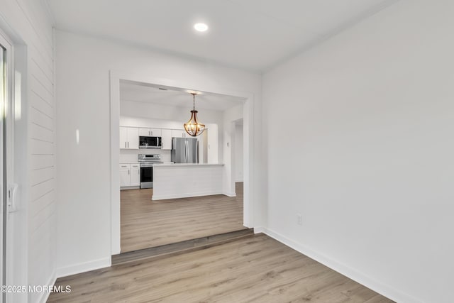 kitchen featuring pendant lighting, white cabinetry, a chandelier, stainless steel appliances, and light hardwood / wood-style flooring