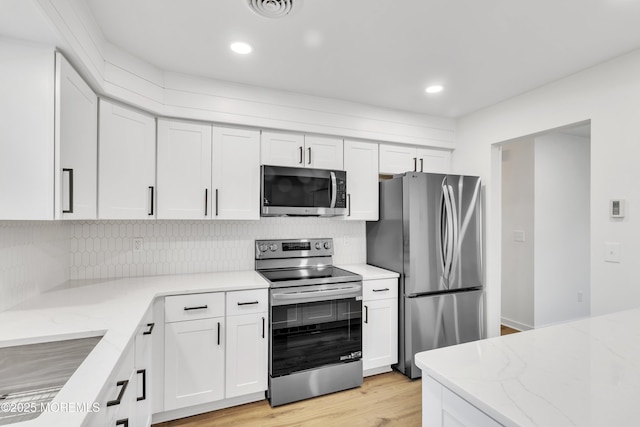 kitchen featuring white cabinetry, light stone counters, light wood-type flooring, stainless steel appliances, and decorative backsplash