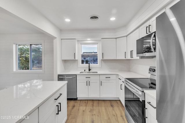 kitchen with light wood-type flooring, stainless steel appliances, sink, and white cabinets