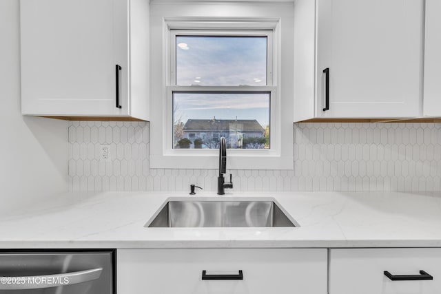 kitchen with stainless steel dishwasher, light stone countertops, sink, and white cabinets