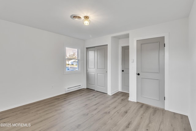 unfurnished bedroom with a closet, light hardwood / wood-style flooring, and a baseboard heating unit