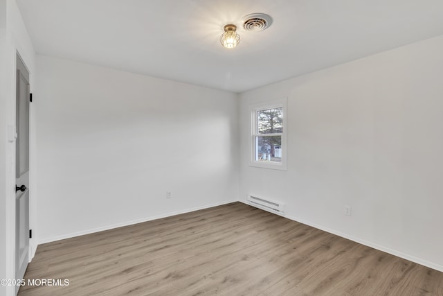 spare room featuring a baseboard heating unit and light hardwood / wood-style floors