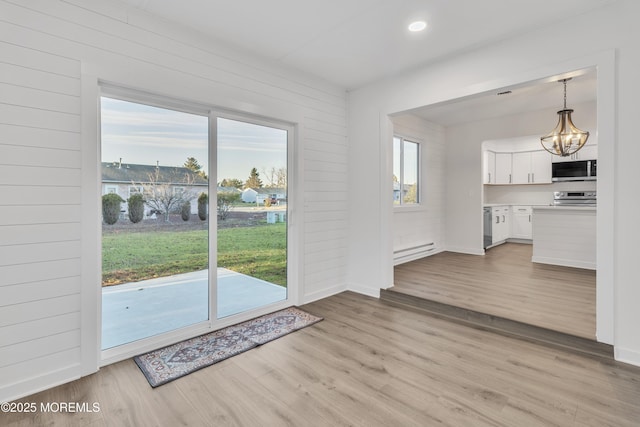 interior space with a baseboard radiator, a chandelier, light hardwood / wood-style flooring, and wood walls