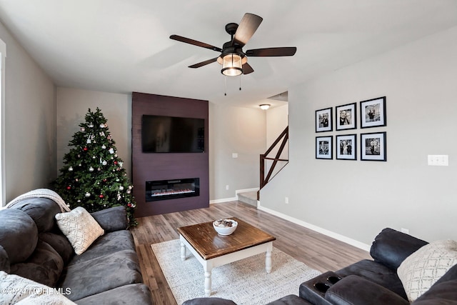 living room featuring ceiling fan, a large fireplace, and wood-type flooring