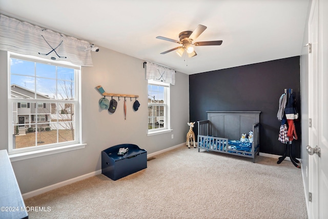 carpeted bedroom featuring a nursery area and ceiling fan