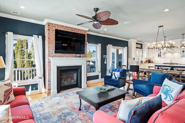 living room featuring ceiling fan with notable chandelier, sink, crown molding, light hardwood / wood-style flooring, and a large fireplace