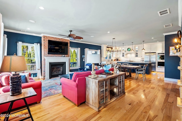 living room featuring ceiling fan, a large fireplace, light hardwood / wood-style floors, and ornamental molding