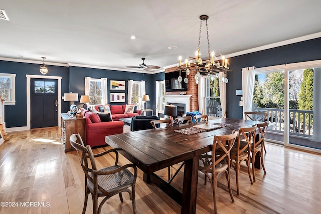 dining room featuring crown molding, a large fireplace, light hardwood / wood-style floors, and ceiling fan with notable chandelier