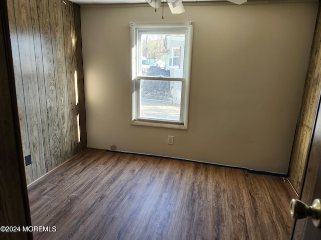 spare room featuring ceiling fan, dark wood-type flooring, and wood walls