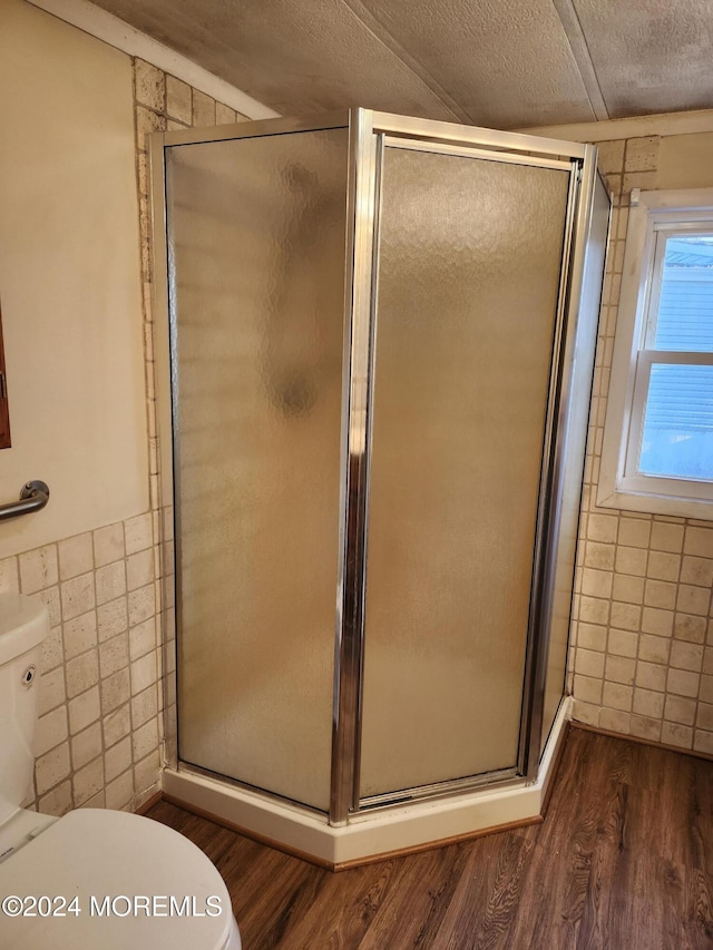 bathroom featuring wood-type flooring, a textured ceiling, an enclosed shower, toilet, and tile walls