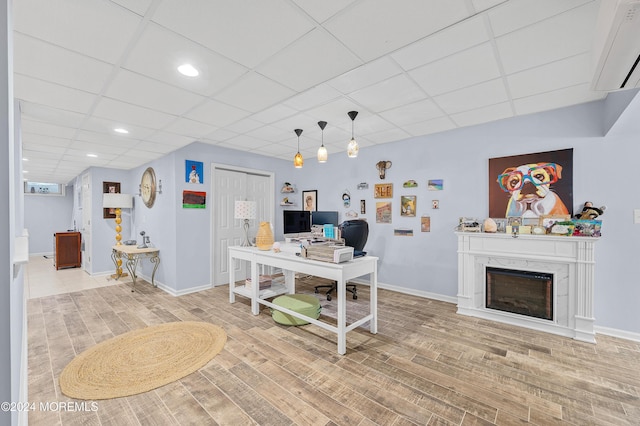 office with hardwood / wood-style floors, a paneled ceiling, an AC wall unit, and a fireplace