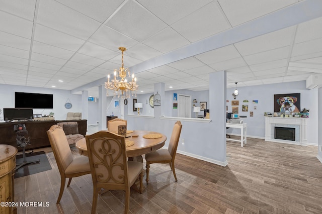 dining area featuring a fireplace, wood-type flooring, a paneled ceiling, and an inviting chandelier