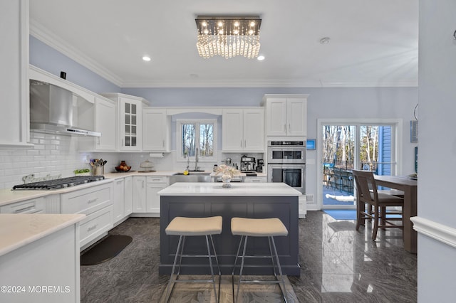 kitchen with wall chimney exhaust hood, a healthy amount of sunlight, white cabinets, and stainless steel appliances