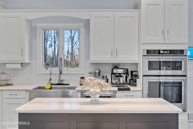 kitchen with white cabinets, stainless steel double oven, and backsplash