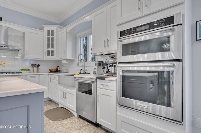 kitchen featuring tasteful backsplash, white cabinetry, stainless steel appliances, and wall chimney range hood